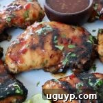 Grilled Thai glazed chicken thighs are topped with fresh herbs on a white plate. A small bowl of dipping sauce is visible on the side.