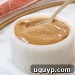 A small white ceramic bowl filled with smooth Thai peanut dressing with a spoon dipping in, ready to be served.