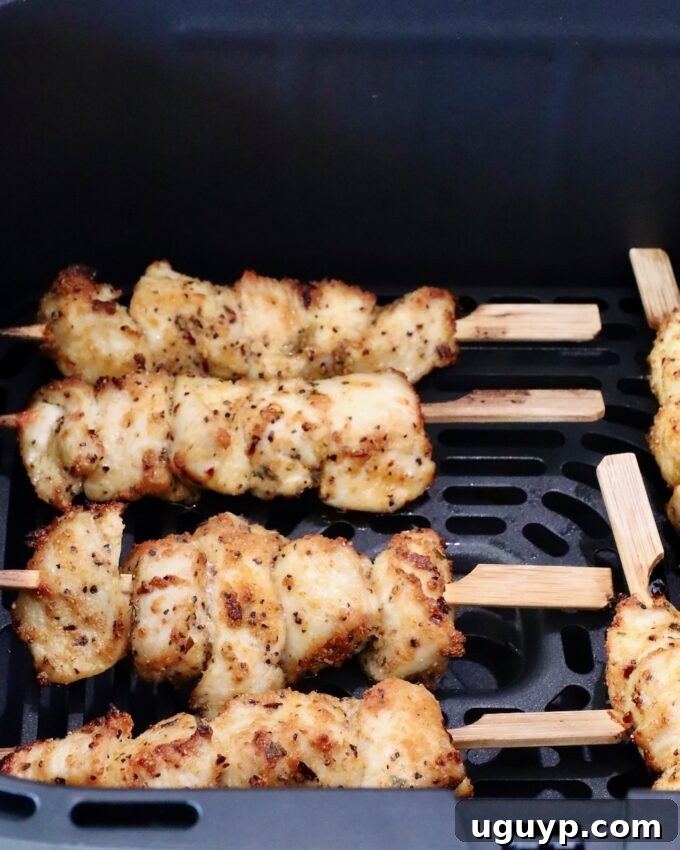 Cooked golden-brown chicken skewers, perfectly seared and seasoned, resting in an air fryer basket after the initial cooking phase.