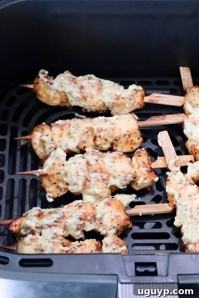 Cooked chicken skewers generously coated with creamy garlic parmesan sauce, still in the air fryer basket, ready for a final quick cook.