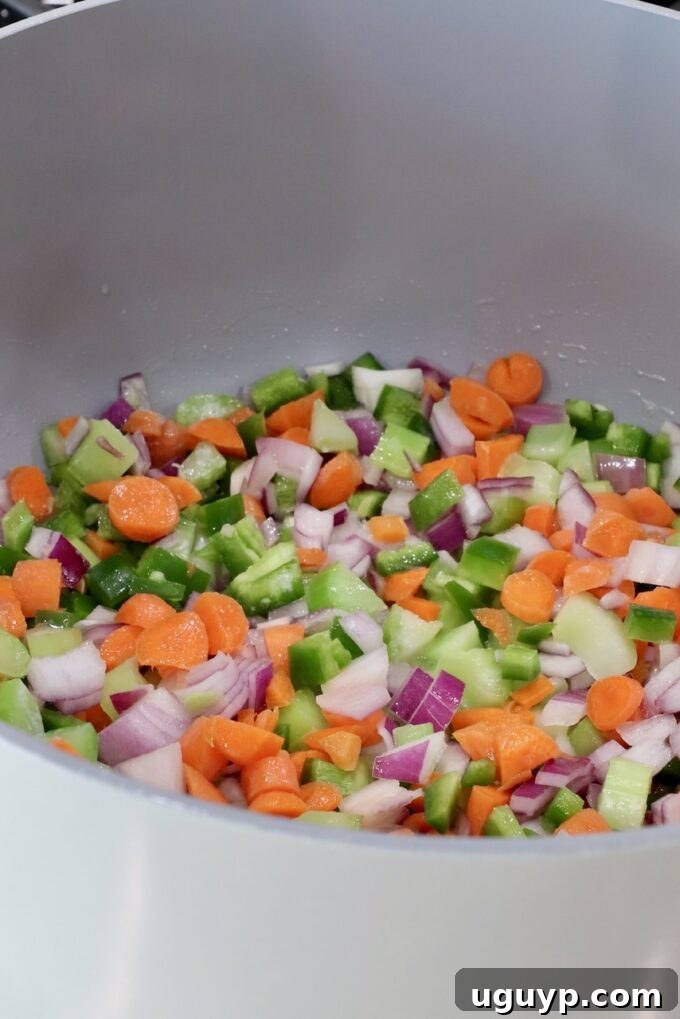 Chopped vegetables, including carrots, green peppers, onions, and celery, in a large gray pot