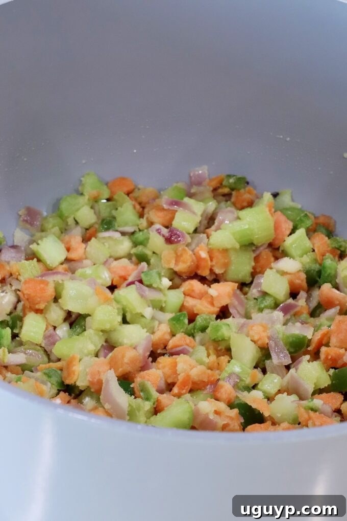 Chopped vegetables, including carrots, jalapeno peppers, onions, and celery, in a large gray pot, covered in flour