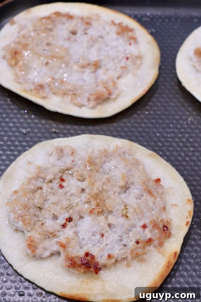 Smash tacos cooking on a griddle with the seasoned meat side facing up, showing the delicious crust forming.