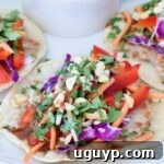 Close-up of pad thai tacos with vibrant toppings like red peppers, carrots, purple cabbage, and cilantro, highlighting the fresh ingredients.