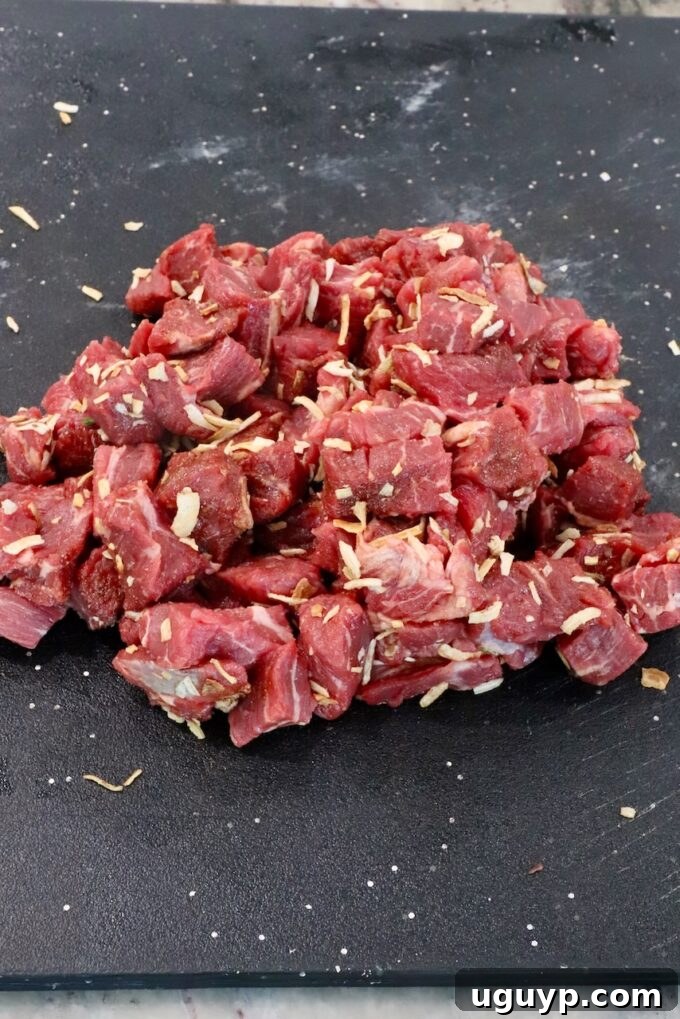 Perfectly cubed beef chuck roast generously coated with French onion seasoning, ready for searing on a black cutting board.