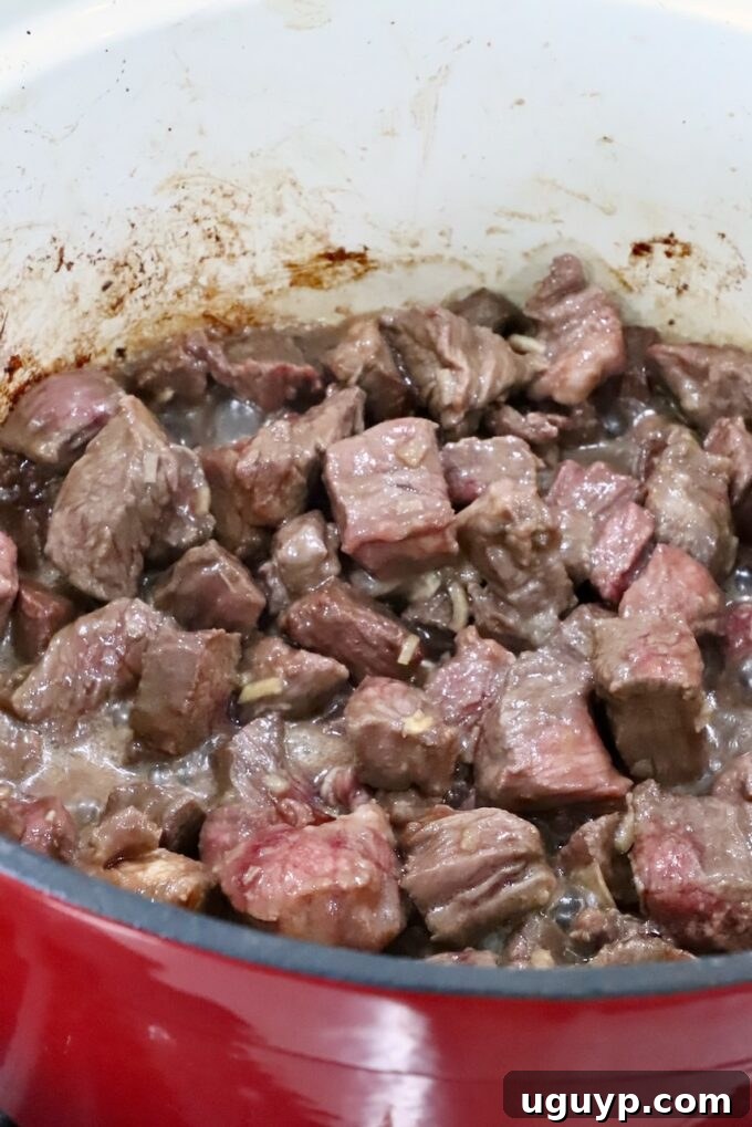 Beautifully seared pieces of beef developing a rich brown crust in a large, hot Dutch oven on the stovetop.