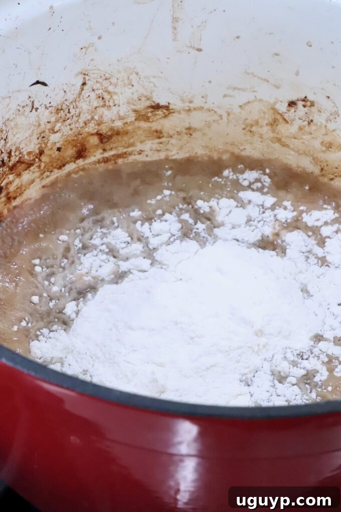 All-purpose flour being stirred into the beef drippings and a small amount of beef stock in the bottom of a large pot, forming a roux.