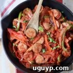 cooked sliced bell peppers and sausage in skillet with wooden spoon, ready to serve