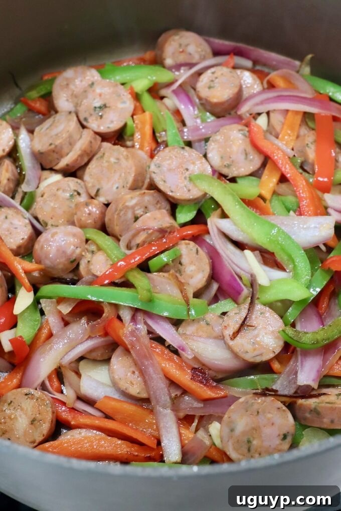 sliced Italian sausage and bell peppers in a large pan cooking