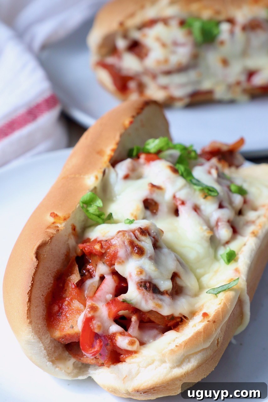 sausage and peppers in sub sandwich topped with melted mozzarella cheese on white plate, ready to eat