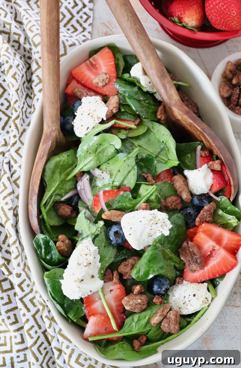 Large, colorful spinach strawberry salad in a serving bowl, garnished with fresh sliced strawberries, dollops of ricotta cheese, and chopped pecans.