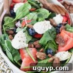 Spinach salad in a large bowl topped with berries, pecans, and ricotta cheese