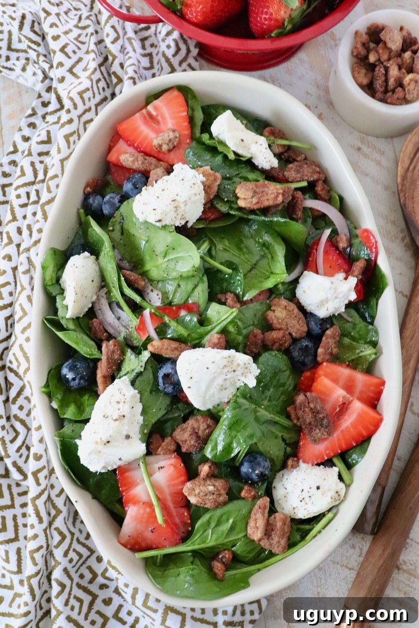 Beautifully presented spinach strawberry salad in a large serving bowl, generously topped with fresh strawberries and dollops of creamy ricotta cheese.