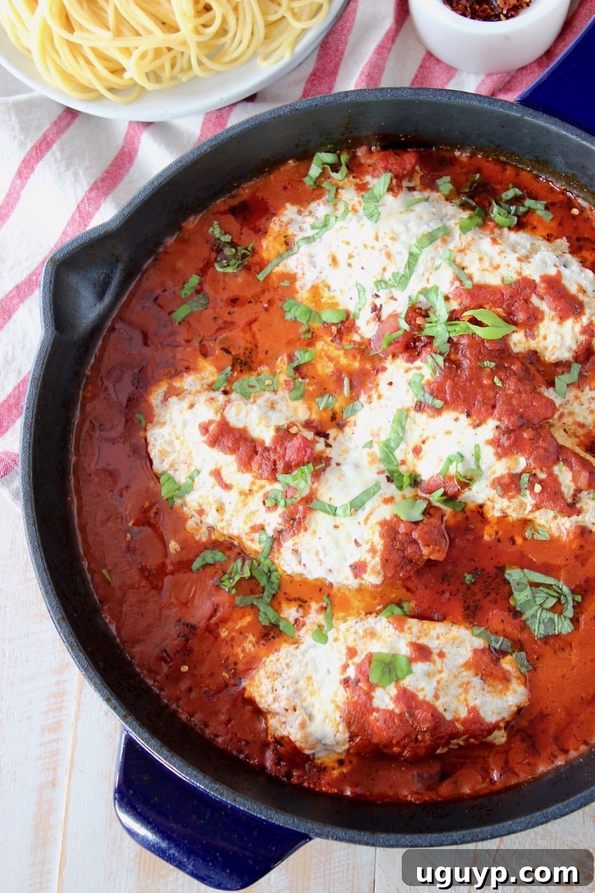 A large cast iron skillet filled with golden, gluten-free chicken parmesan, smothered in rich marinara sauce and topped with melted cheese, with a bowl of spaghetti noodles on the side.