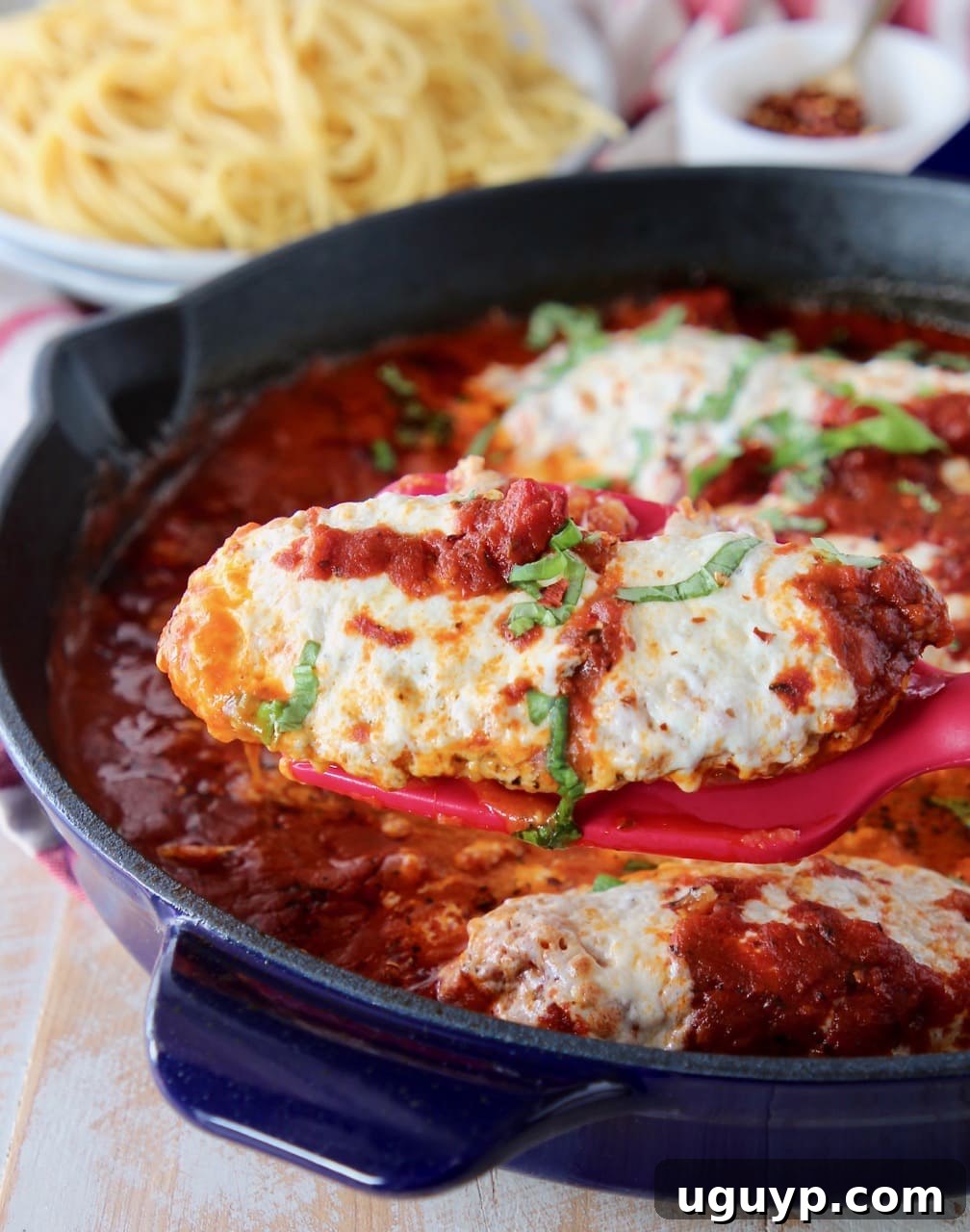 A close-up shot of a spatula expertly lifting a piece of baked gluten-free, low-carb chicken parmesan from a hot skillet, highlighting its rich marinara and melted mozzarella.