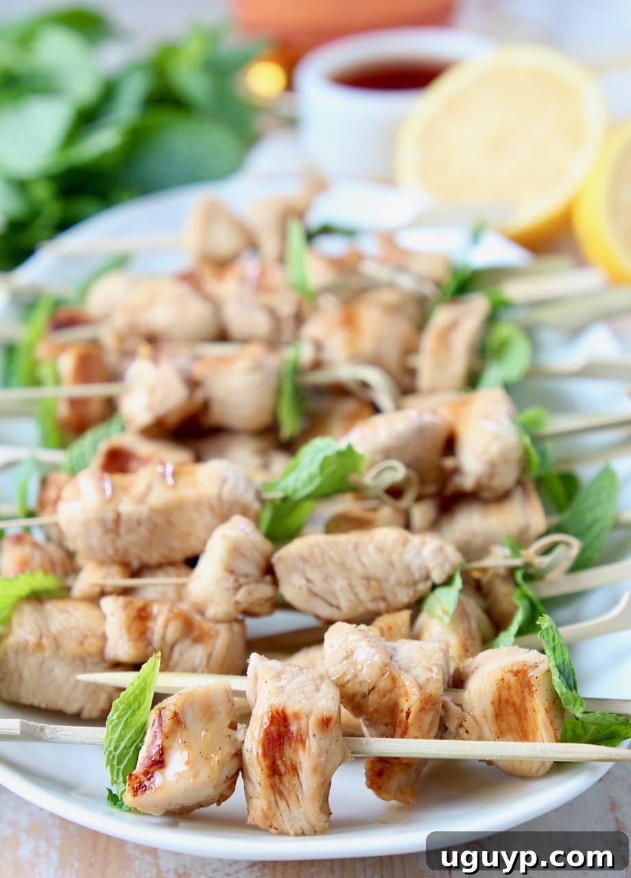 Grilled chicken pieces on small wooden skewers with fresh mint leaves, sitting on a white oval plate