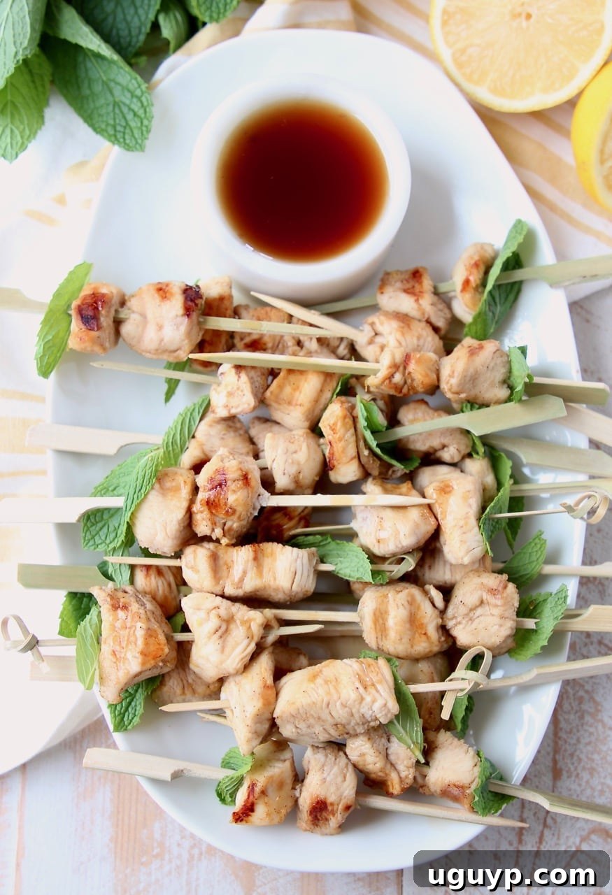 Overhead shot of chicken skewers on white plate with small bowl of bourbon sauce on the side