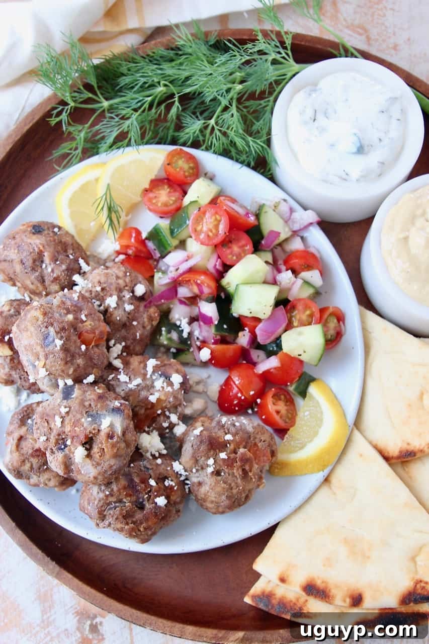 Greek meatballs on plate with tomato cucumber salad and slices of pita bread on the side