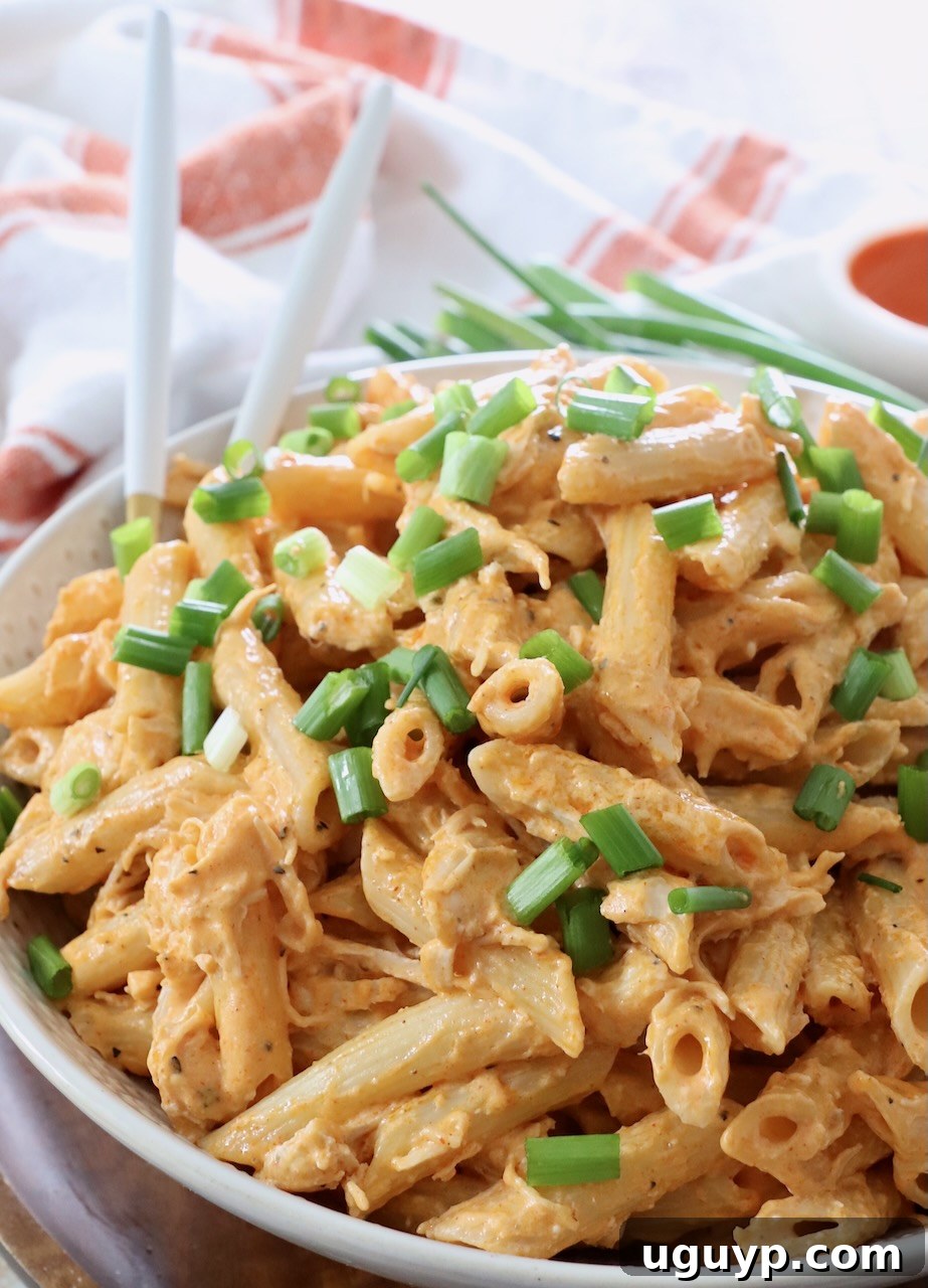 Two forks ready to serve a large bowl of Buffalo Chicken Pasta, topped with fresh green onions, highlighting its creamy texture.