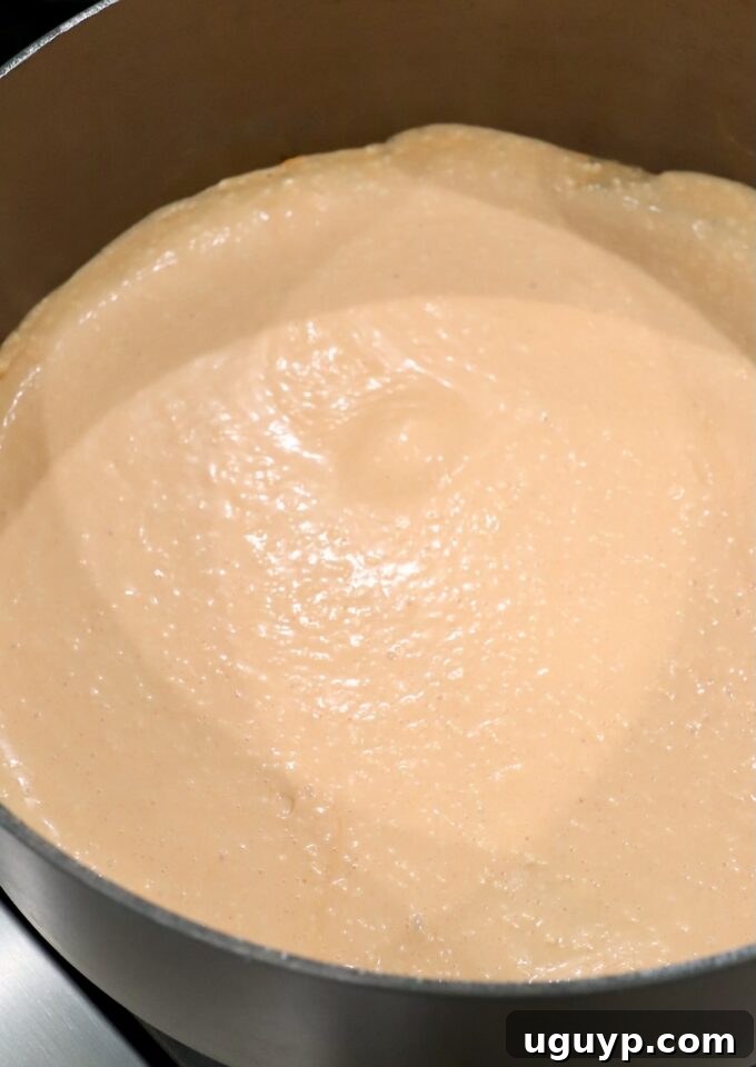 The buffalo sauce base simmering and becoming creamy in a large pot on the stove, showing its rich, orange hue.