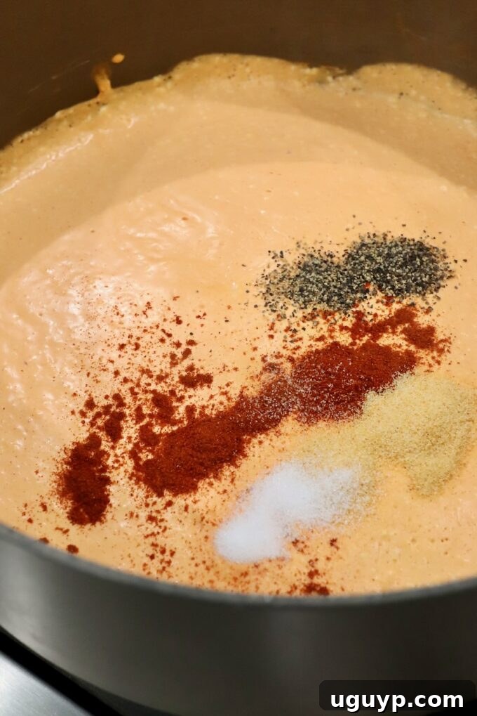 A creamy buffalo sauce in a large pot, with added spices like paprika and garlic powder, ready to be stirred in.