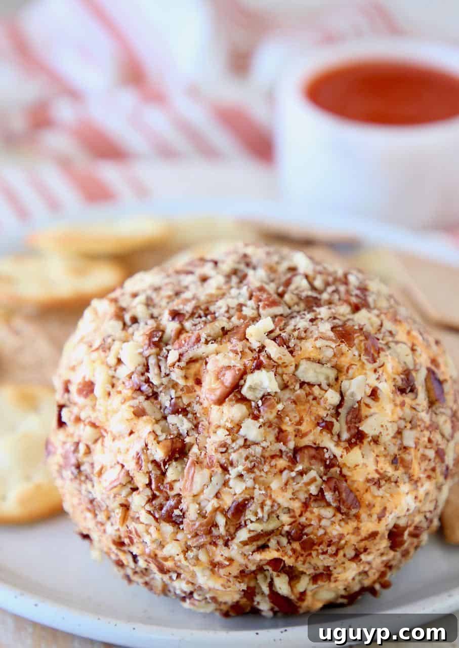 A festive Buffalo Cheddar Cream Cheese Ball coated in pecans, served on a plate with an assortment of crackers.