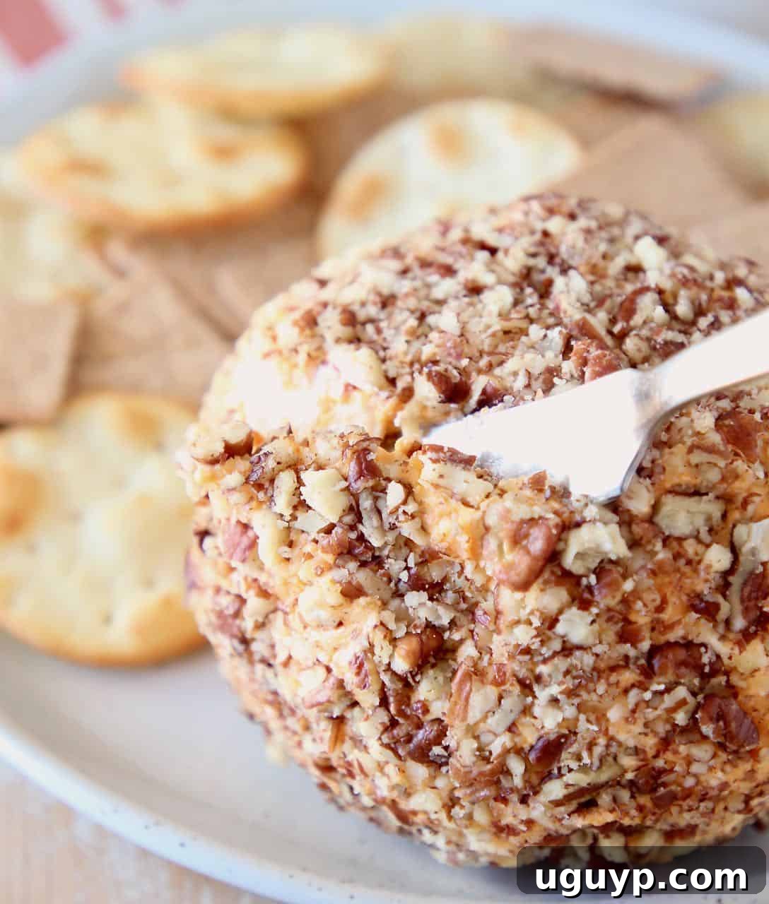A Buffalo Cheddar Cream Cheese Ball being sliced with a cheese knife, showcasing its creamy interior.
