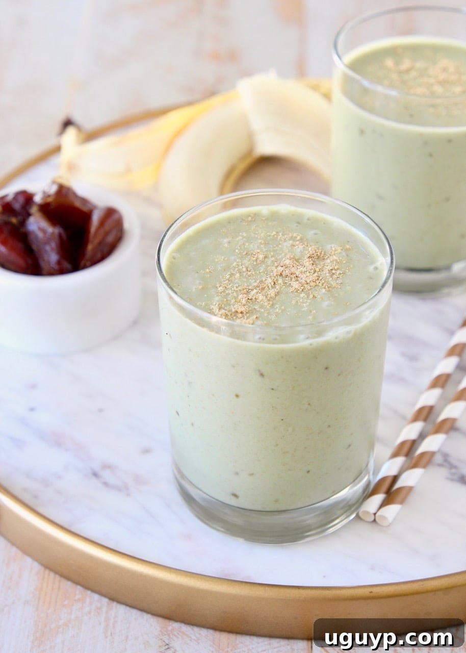 Banana protein shake in two glasses sitting on white marble tray with gold and white striped straws and peeled banana in background