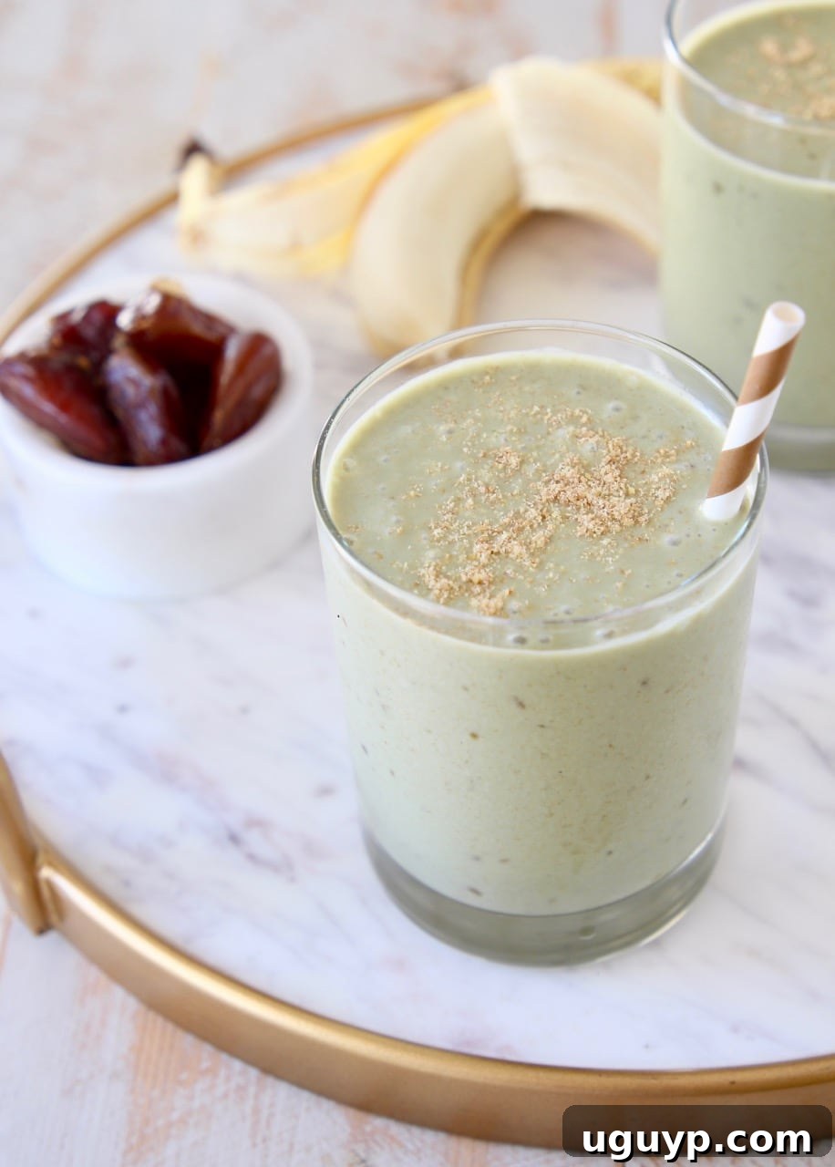 Banana protein shake in glass with gold and white striped straw and ground flaxseed on top with peeled banana in background