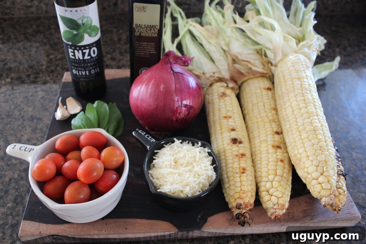 Fresh ingredients for Italian Corn Salad laid out: grilled corn on the cob, cherry tomatoes, red onion, olive oil, balsamic vinegar, garlic, fresh basil, and Parmesan cheese.