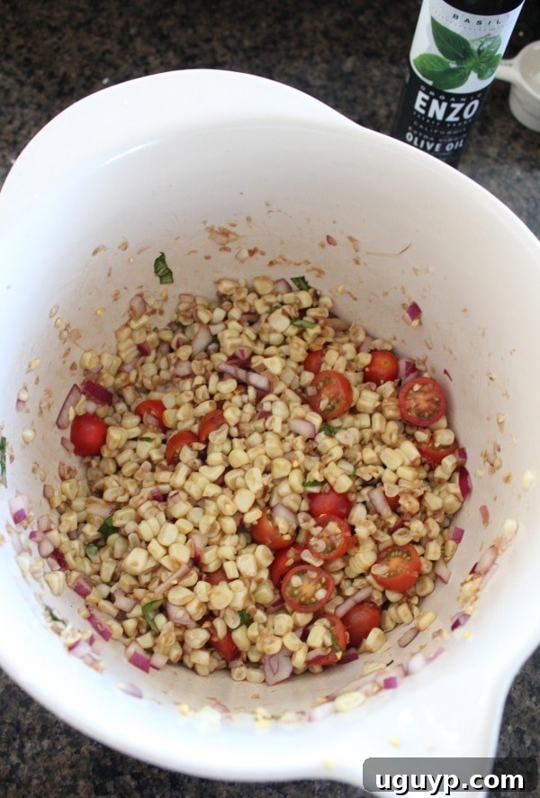The dressing being poured over the corn, tomato, and red onion mixture in a large bowl before tossing.