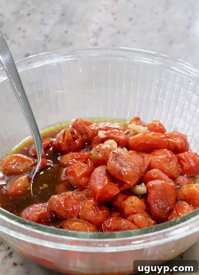 roasted cherry tomatoes with garlic and balsamic vinegar in a glass bowl with a spoon