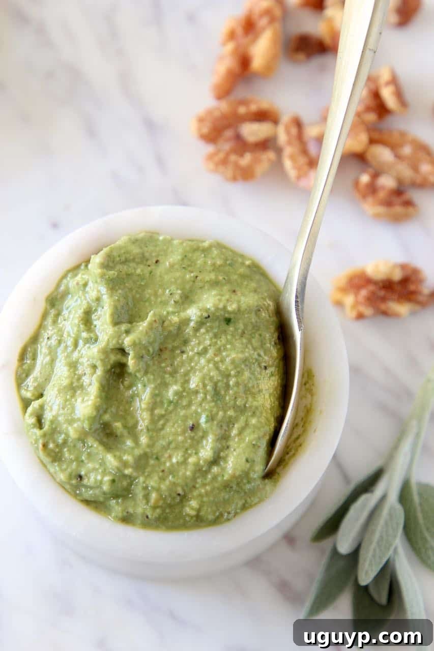 Fresh homemade Walnut Sage Pesto in a white marble bowl with a small gold spoon, ready to be served. Vegan, paleo, and Whole30 friendly.