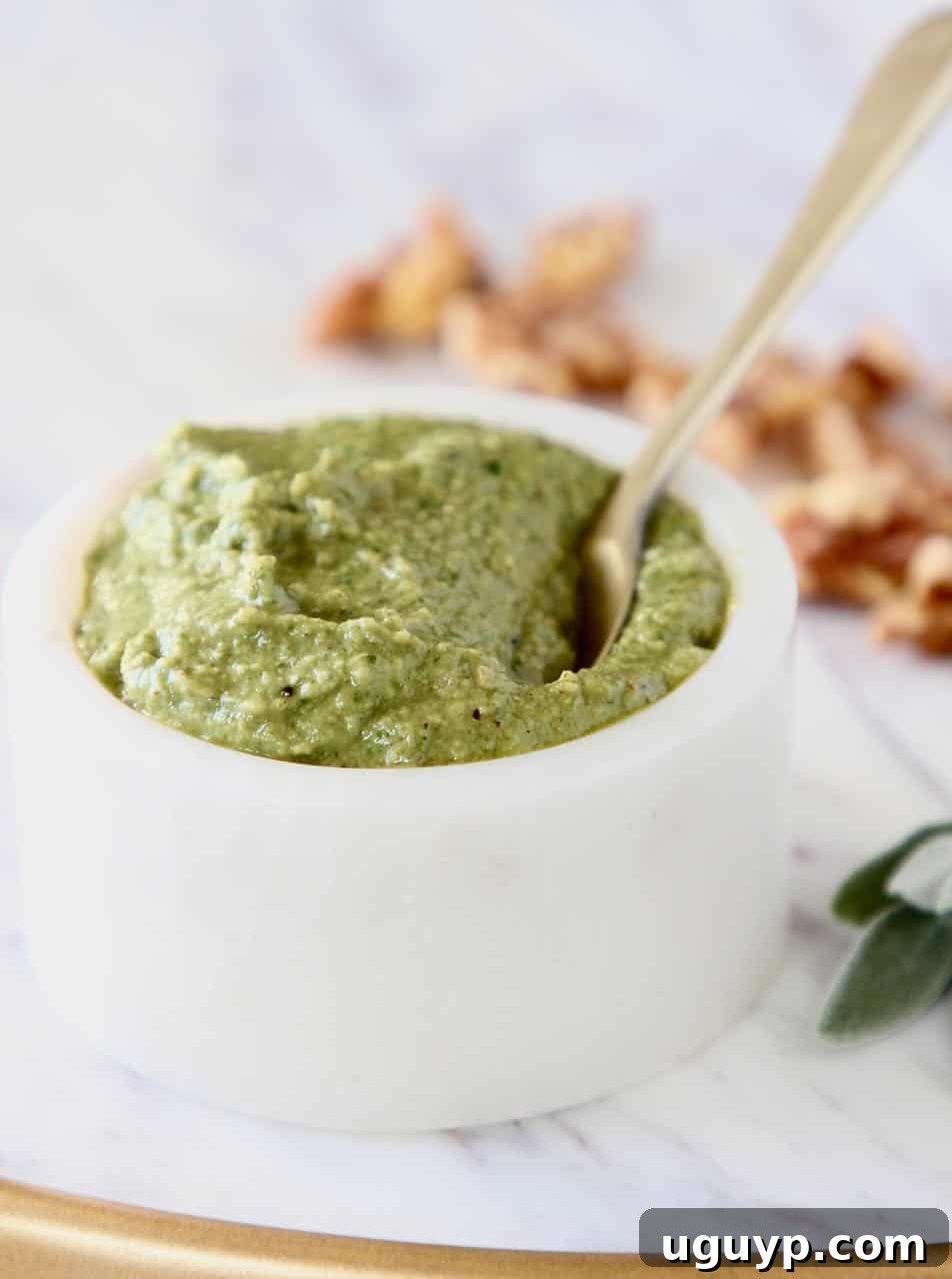 Fresh homemade Sage Pesto in a pristine white bowl with a golden spoon, showcasing its rich texture. This 5-minute recipe is vegan, paleo, and Whole30 friendly.