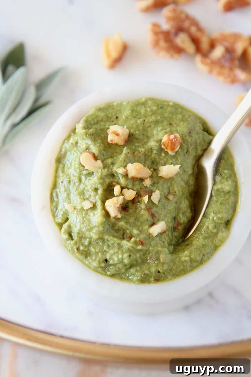 Sage pesto in a white bowl, generously topped with freshly chopped walnuts, ready for serving. A healthy and flavorful homemade sauce.
