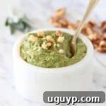 Sage pesto in marble white bowl with gold spoon, topped with chopped walnuts, a healthy and delicious homemade sauce.