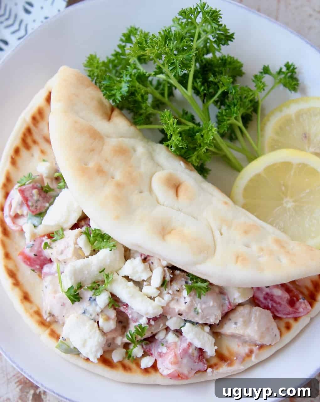 Overhead view of Greek Chicken Salad served in warm pita bread with lemon wedges and fresh parsley