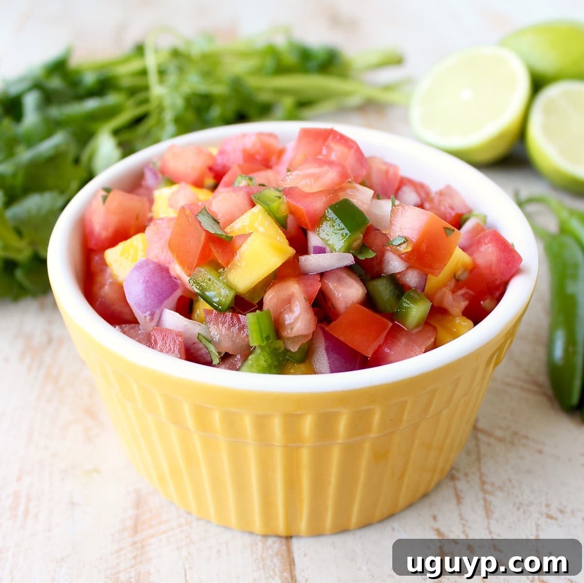 A vibrant yellow bowl brimming with diced mango, ripe tomatoes, crisp red onions, and fiery jalapeños, ready to be mixed into a fresh mango salsa.