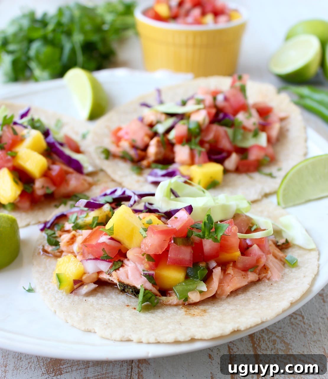 Warm corn tortillas generously topped with perfectly cooked salmon and a fresh, colorful mango salsa, arranged on a white plate.