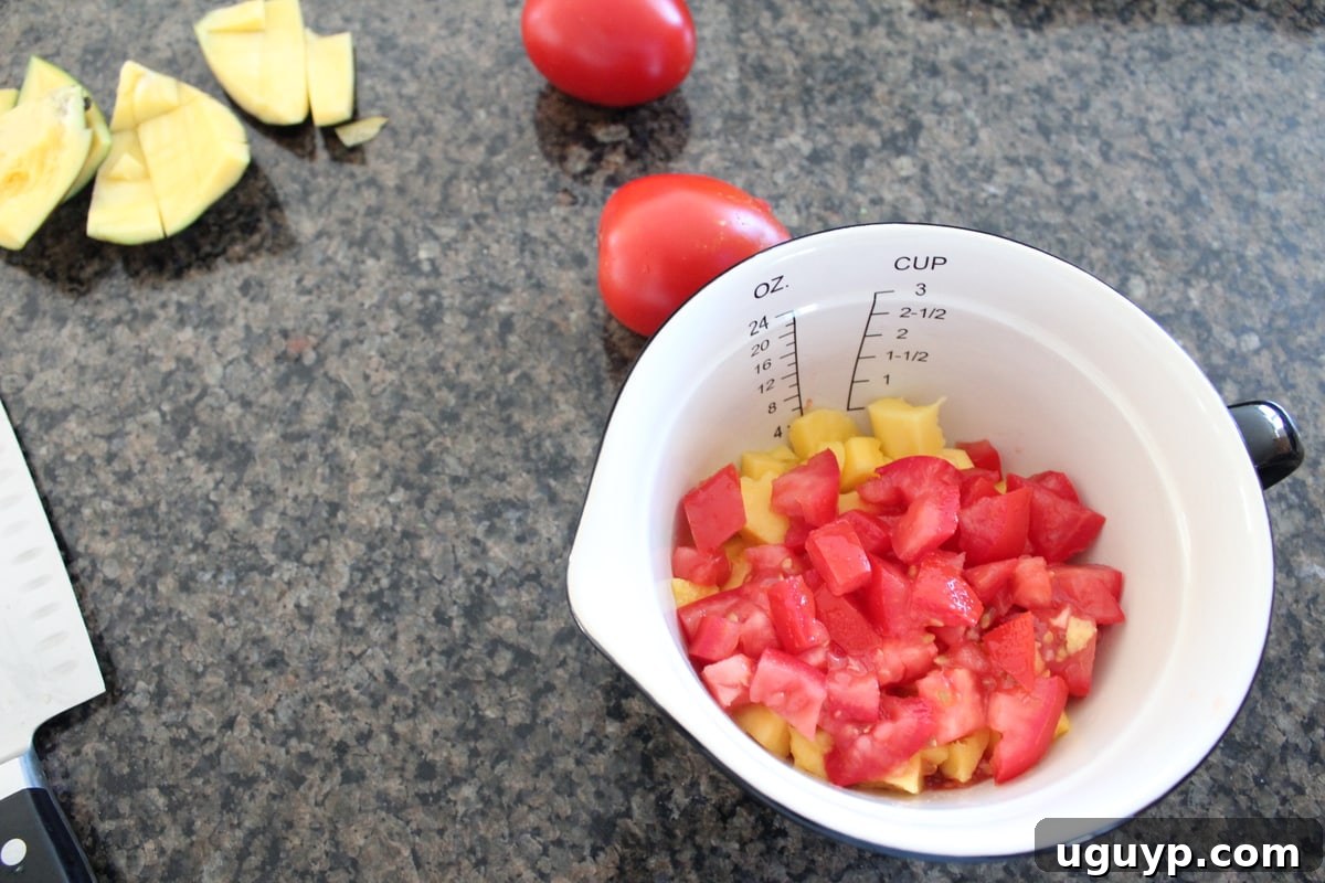 A close-up shot of freshly diced mango and ripe tomatoes, perfectly prepared and combined in a bowl for the salsa base.