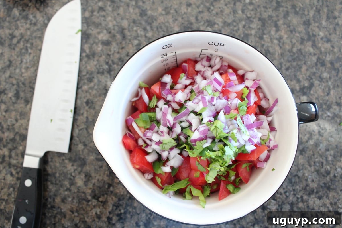The vibrant additions of minced red onion, jalapeño, and chopped fresh cilantro being added to the bowl with mango and tomatoes.