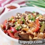 Kung Pao Beef with rice noodles, green onions, and sliced red bell peppers in a large white bowl, garnished with peanuts.