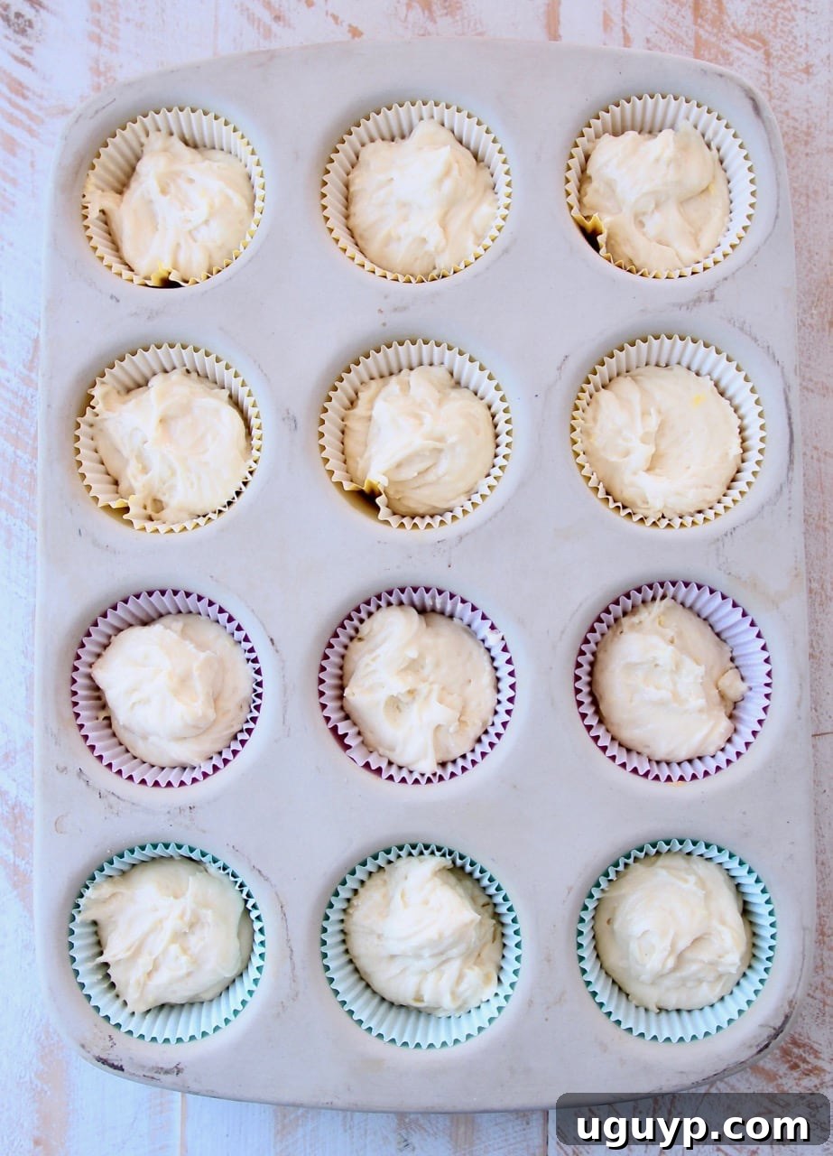 Close-up of unbaked lemon cupcake batter in paper liners within a stone muffin pan, ready for the oven