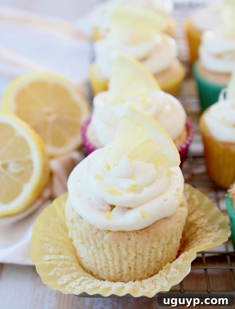 Lemon cupcake with its paper liner unwrapped, showcasing moist cake and topped with lemon cream cheese frosting and a lemon slice