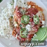 A plate of Mexican chicken parmesan topped with salsa, jalapeño slices, and cheese, served with cilantro rice and avocado slices on the side.