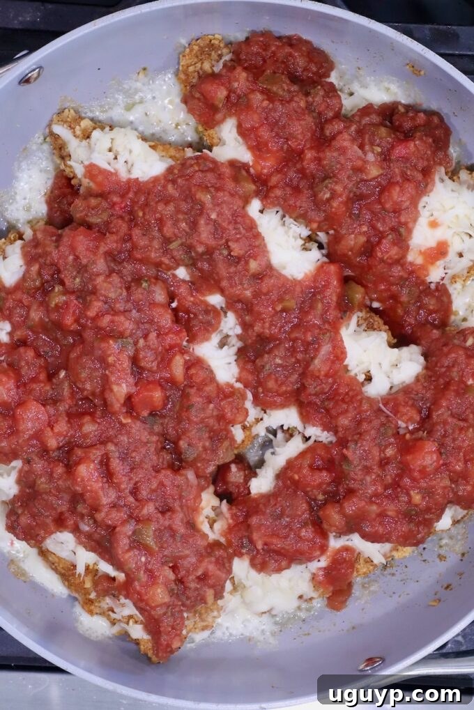Pan-fried breaded chicken breasts topped with melted cheese and chunky salsa in a skillet.