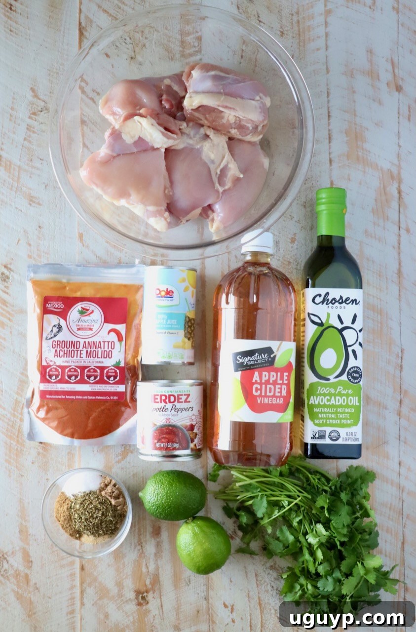 Raw chicken thighs in a bowl surrounded by ground annatto, pineapple juice, chipotle peppers, apple cider vinegar, avocado oil, lime, cilantro, and spices.