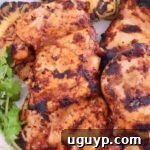 Grilled chicken thighs with charred marks on a white plate, garnished with fresh cilantro.