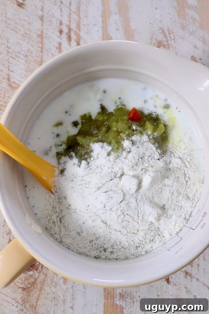 Mixing bowl with ranch dressing mix, buttermilk, and dill pickle relish. A yellow spatula rests in the bowl on a wooden surface. 