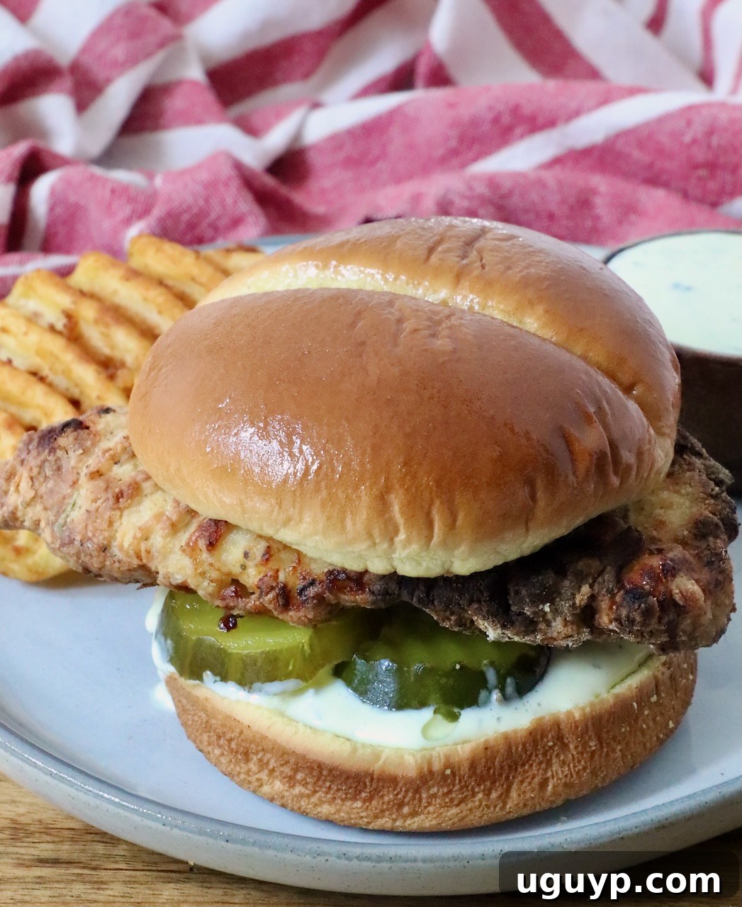 A crispy air fried chicken sandwich on a soft bun with pickles and creamy sauce, served with waffle fries on a plate.
